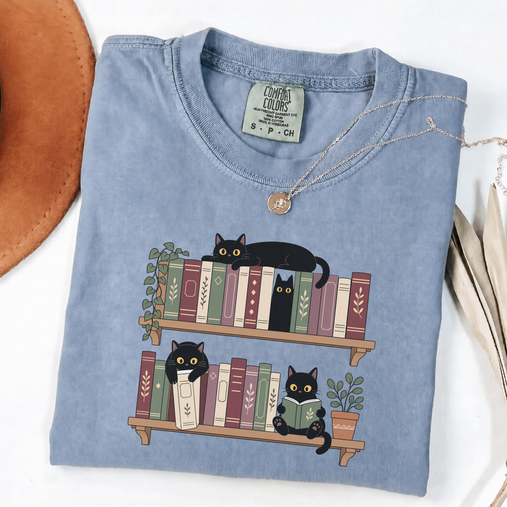 Blue Jean Comfort Colors book-lover shirt featuring black cats among colourful bookshelves