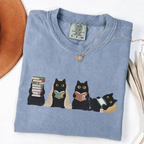 Four black cats with books, a blanket, glasses and an e-reader on a Blue Jean shirt.
