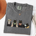 Four black cats with books, a blanket, glasses and an e-reader on a Pepper shirt.