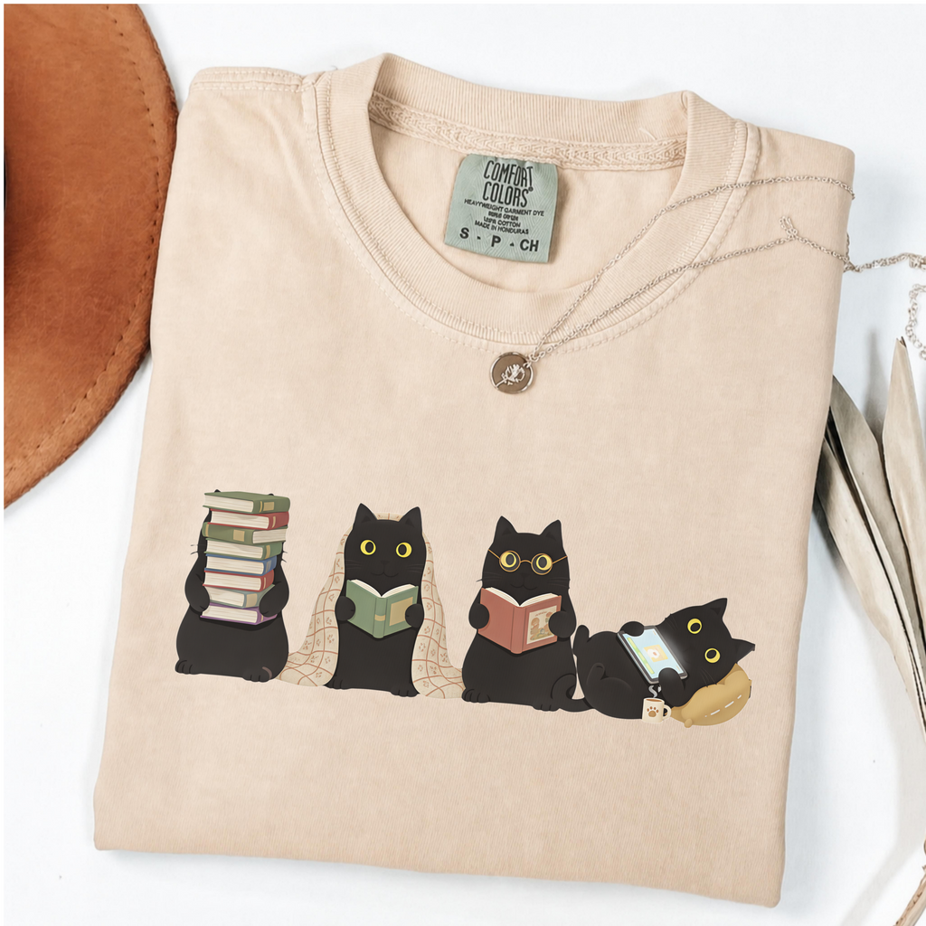 Four black cats with books, a blanket, glasses and an e-reader on a Ivory shirt.