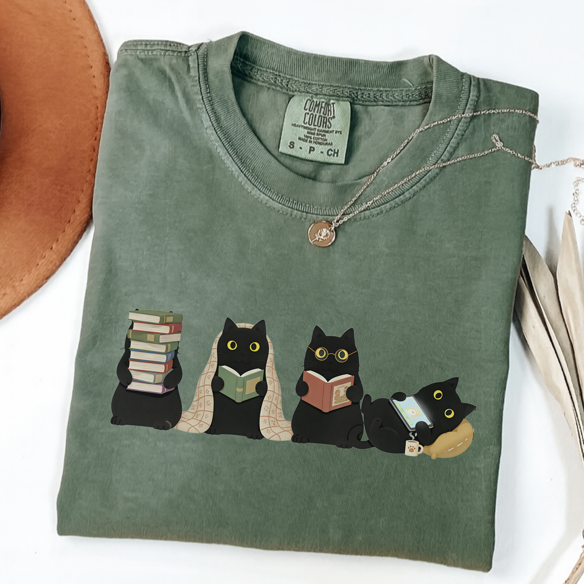 Four black cats with books, a blanket, glasses and an e-reader on a moss shirt.
