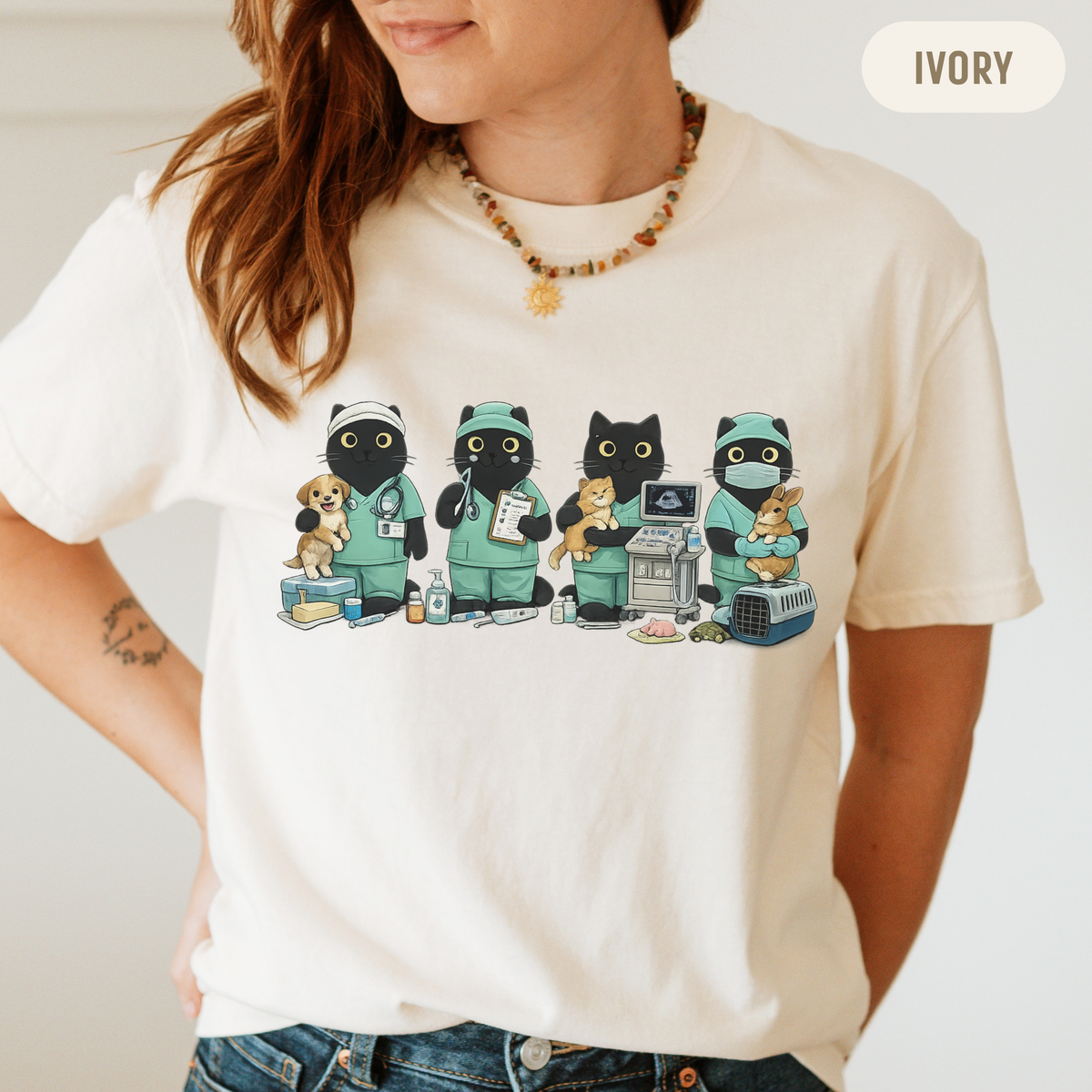 A woman wearing an ivory graphic t-shirt featuring cartoon cats and dogs dressed in green medical scrubs. The image includes an 'IVORY' color label overlay in the top right corner.