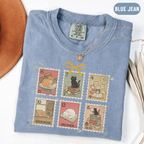 Blue Jean shirt with six vintage-style postage stamps featuring cats reading and resting on books.