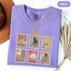 Violet shirt with six vintage-style postage stamps featuring cats reading and resting on books.