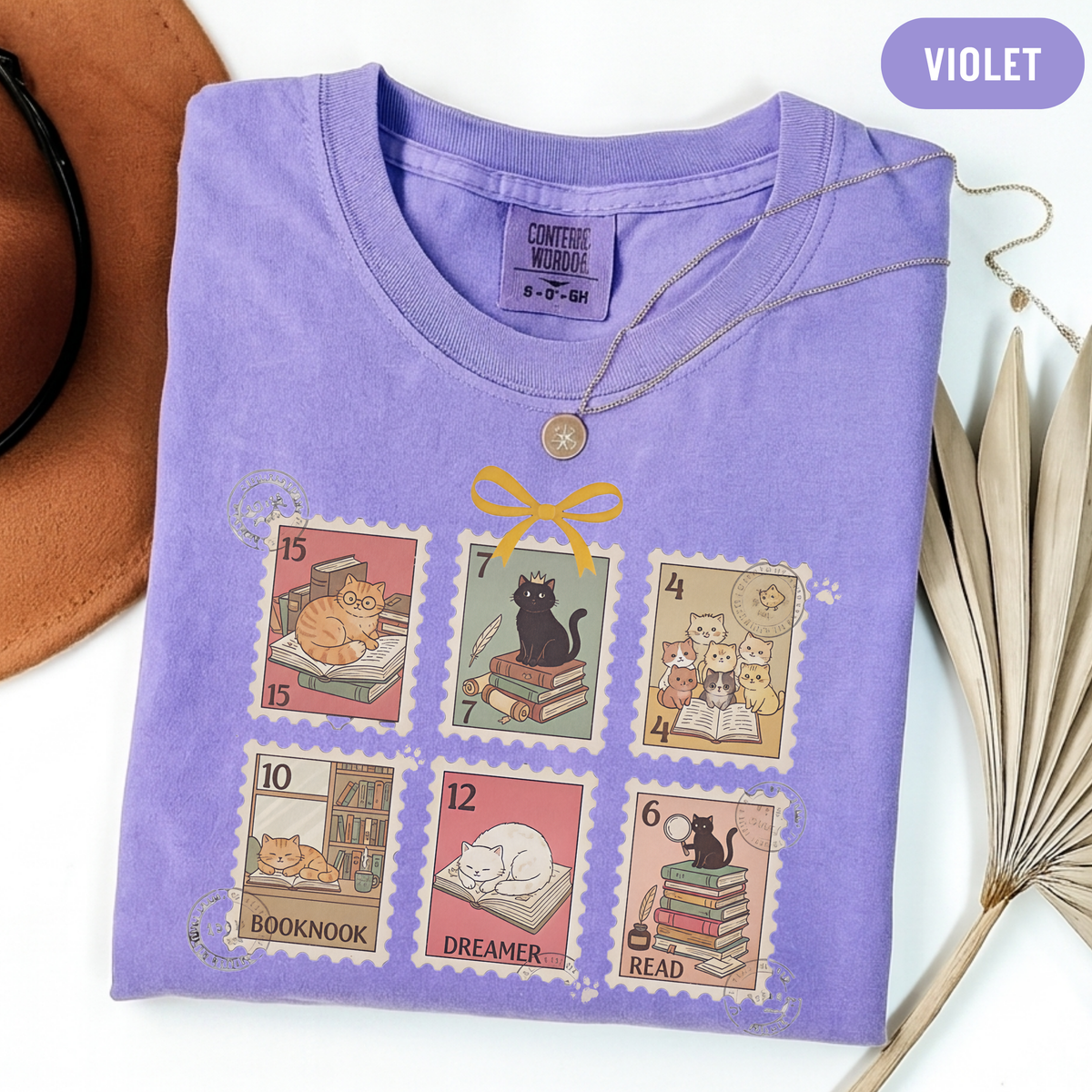 Violet shirt with six vintage-style postage stamps featuring cats reading and resting on books.