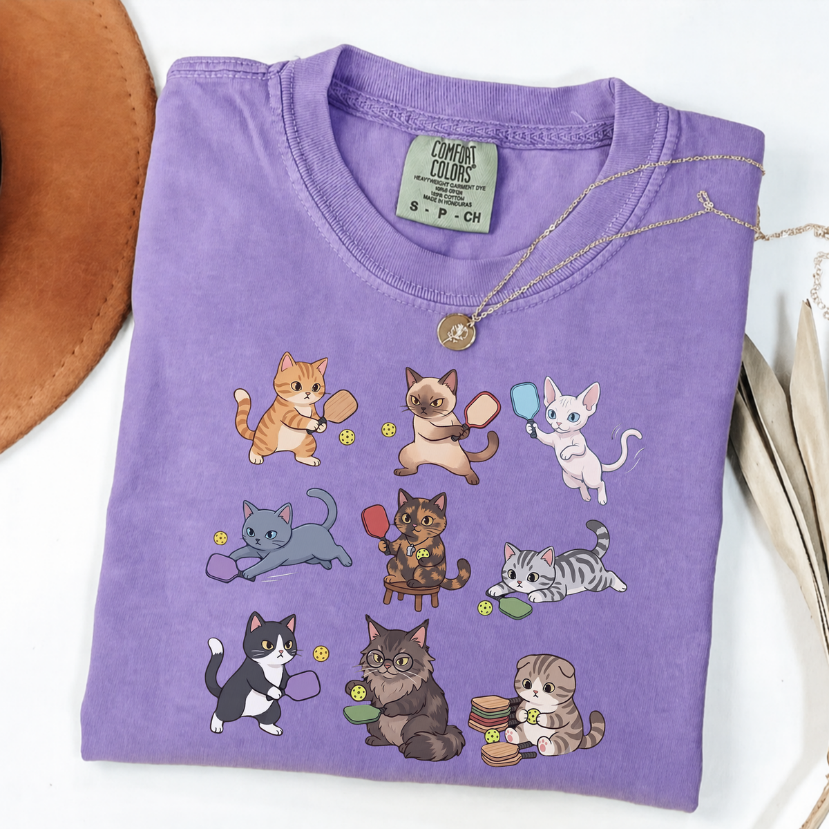 Violet graphic T-shirt with nine cartoon cats playing pickleball