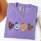 Violet garment-dyed T-shirt featuring four colorful Portuguese folk-art roosters in a row